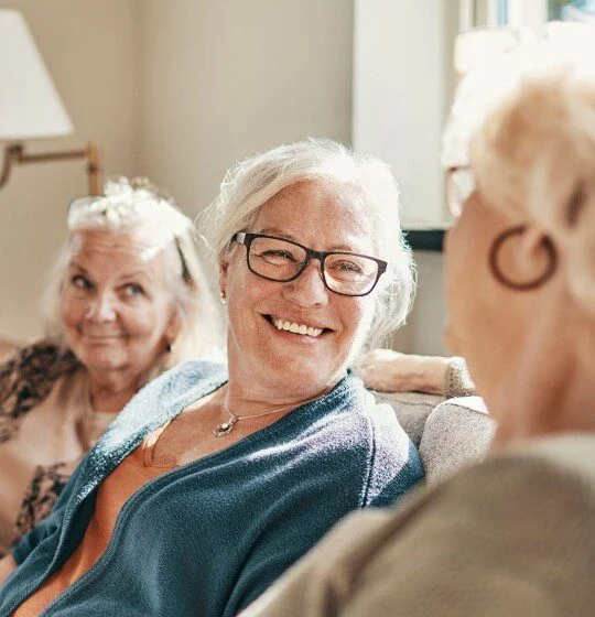 Elderly women chatting and smiling on a sunny day indoors.