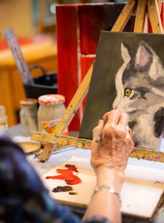 Person painting a cat on a canvas, surrounded by art supplies.