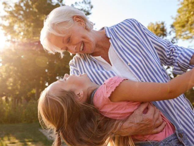 Elderly woman and child smiling and embracing outdoors.