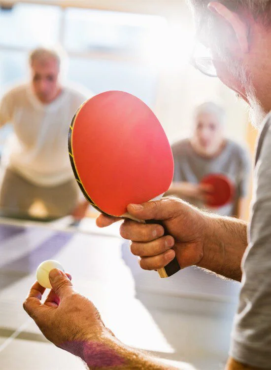 People playing table tennis, focusing on one person holding a paddle and ball.