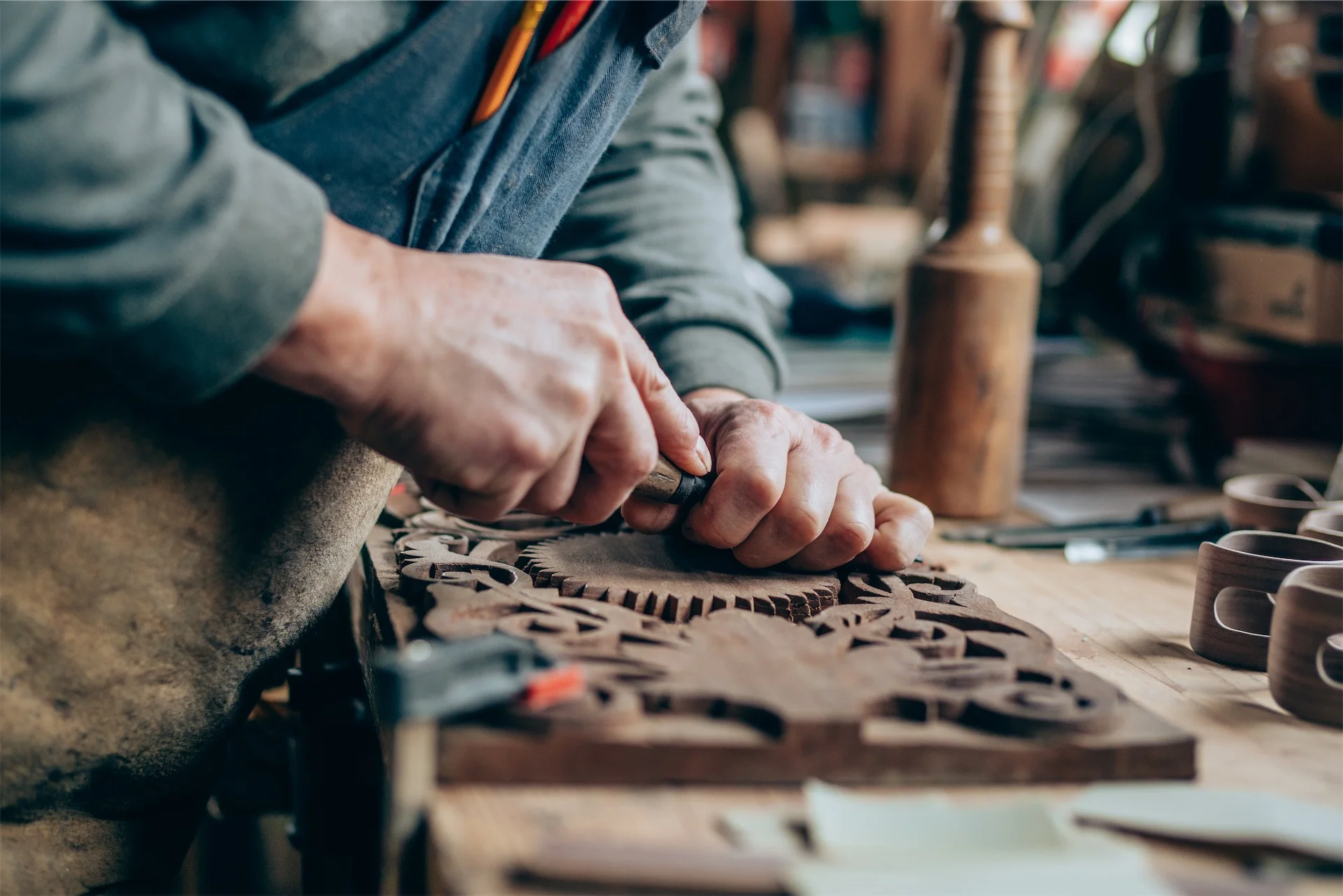 Person carving intricate wood design at a workbench.