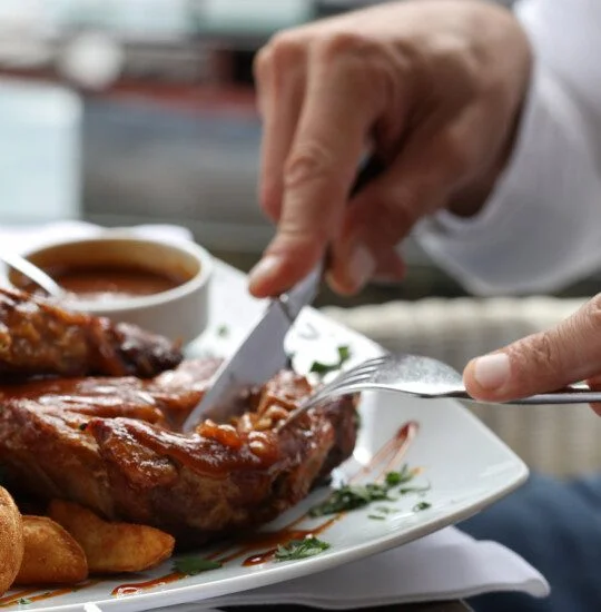 Person slicing steak with sauce and wedges on a plate.
