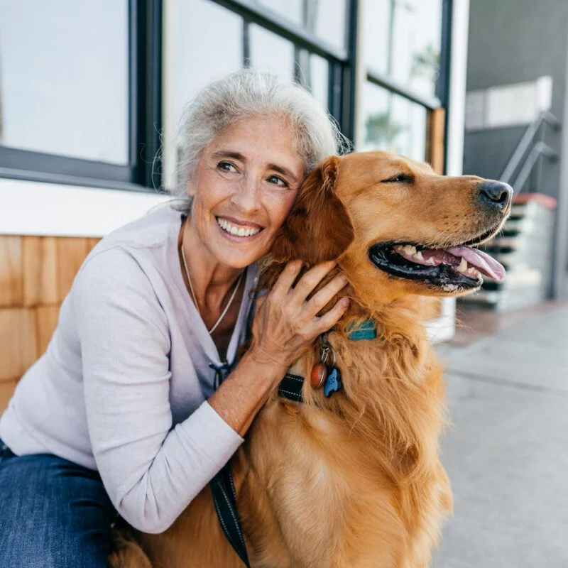 Smiling woman with a golden retriever outside a building.