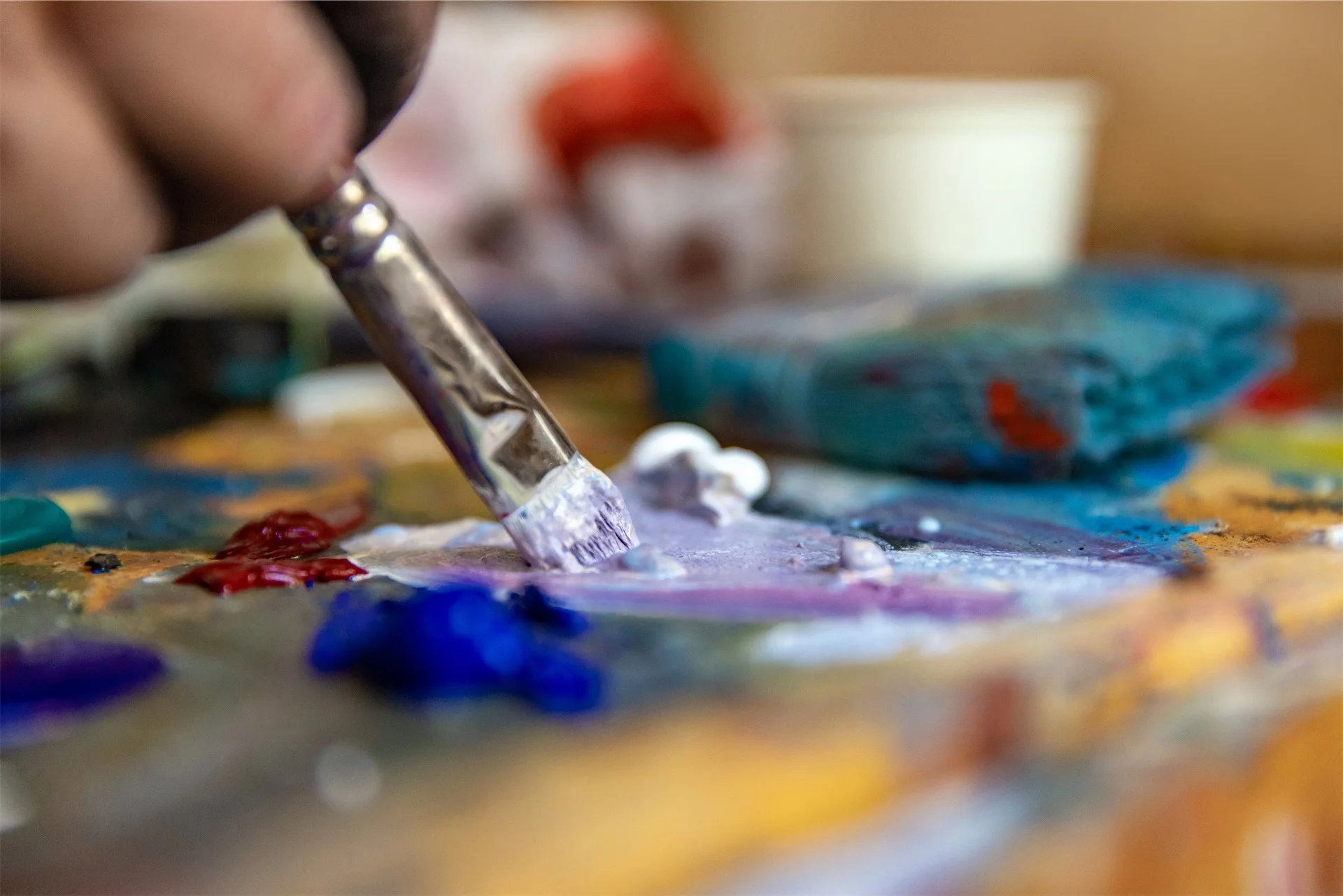 Close-up of a paintbrush mixing colorful paints on a palette.