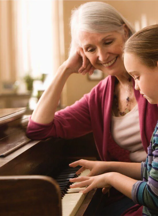 Child learning piano with guidance from an older woman, both smiling.