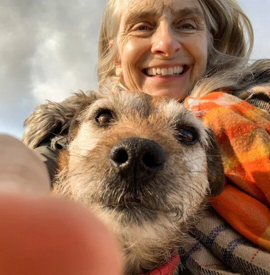 Smiling woman and dog take a cheerful selfie outdoors with a scarf.