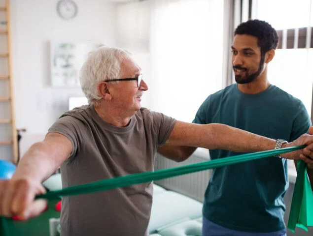 Elderly man exercises with a physiotherapist using a green resistance band.