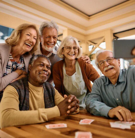 Group of happy seniors taking a selfie at a table with playing cards.