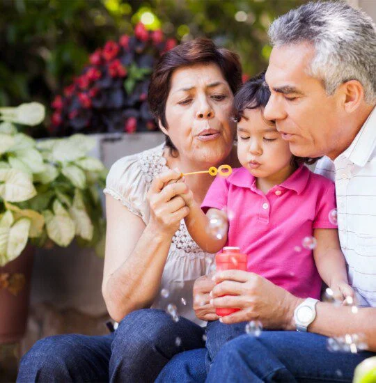 Grandparents and child blowing bubbles together in a garden setting.