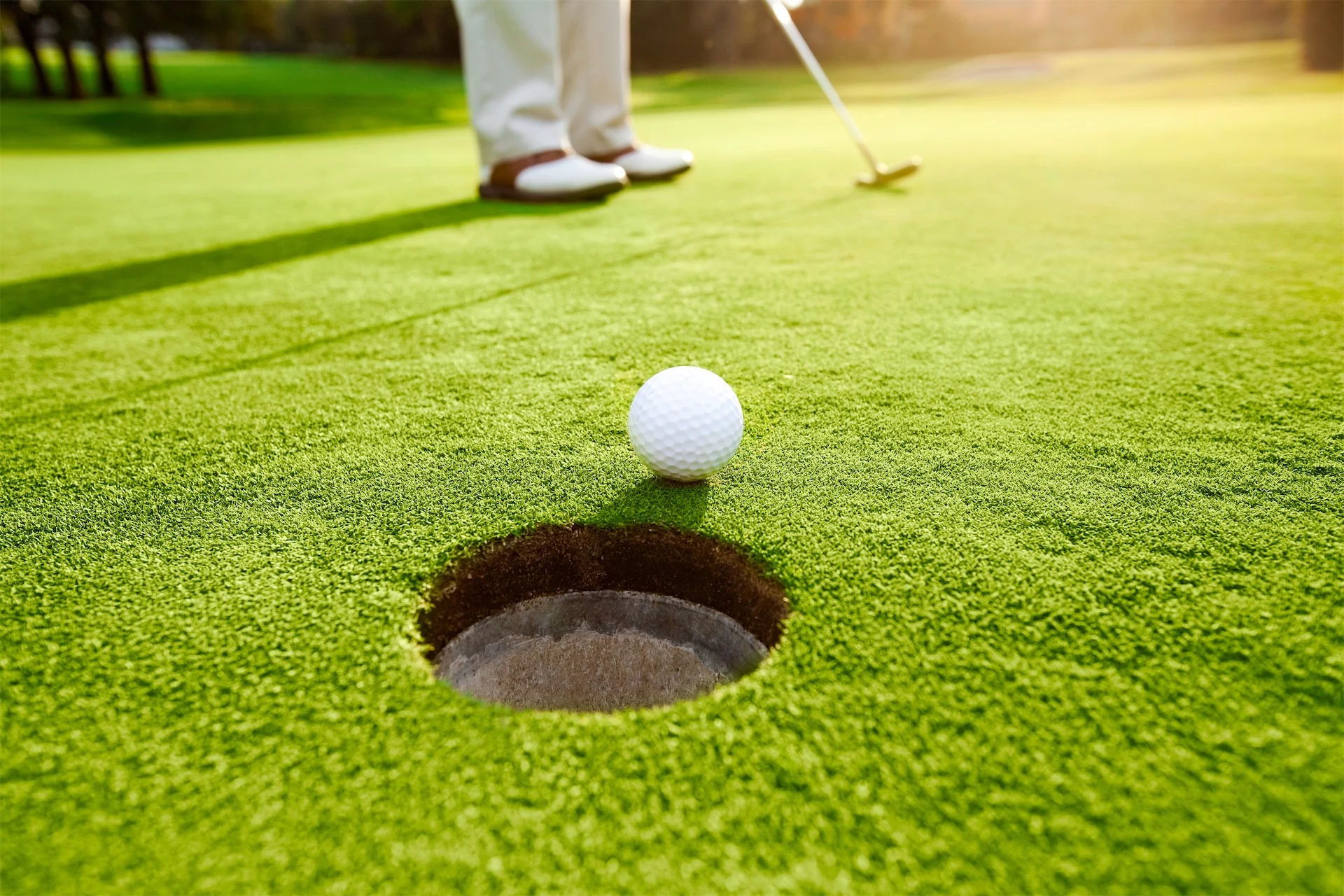 Golf ball near the hole on a sunlit putting green.