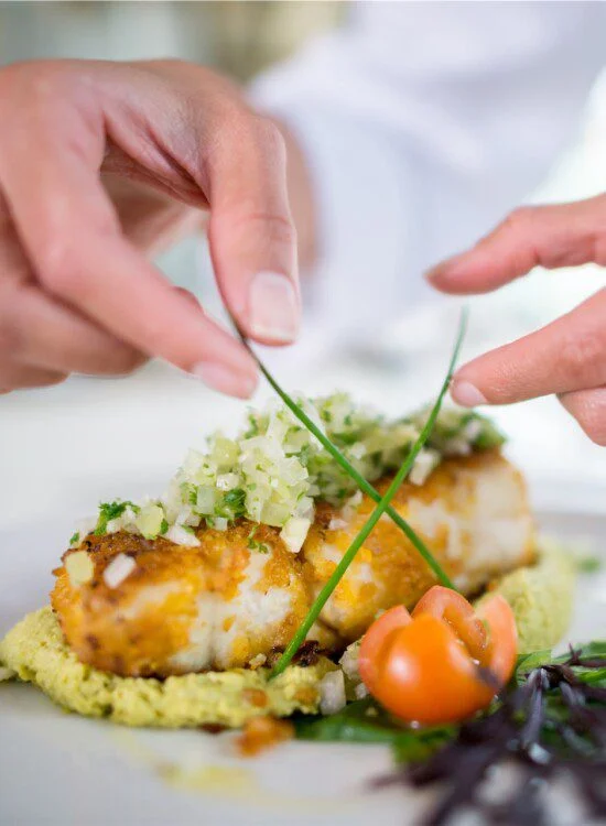 Chef garnishes a dish with herbs and tomatoes on a white plate.