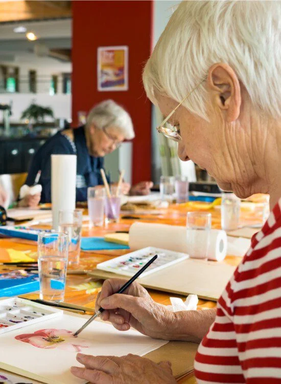 Elderly people painting together at a shared table in a bright art studio.