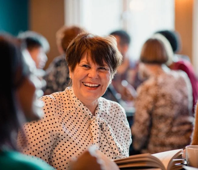 Smiling woman in a group reading a book.
