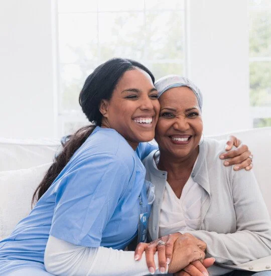 Nurse hugging a smiling patient on a couch in a bright room.