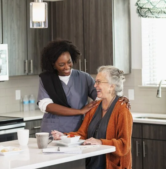 Caregiver and senior woman smiling in a modern kitchen.