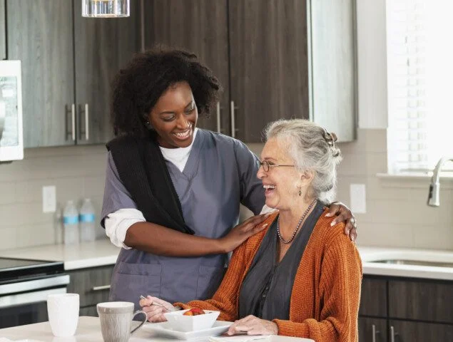 Caregiver and senior woman smiling in a modern kitchen.