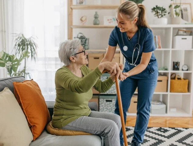 Nurse assists elderly woman with a cane at home.
