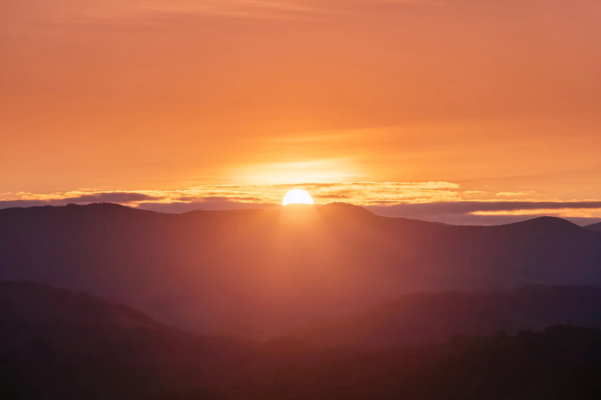 Sunset over mountains with an orange sky and scattered clouds.
