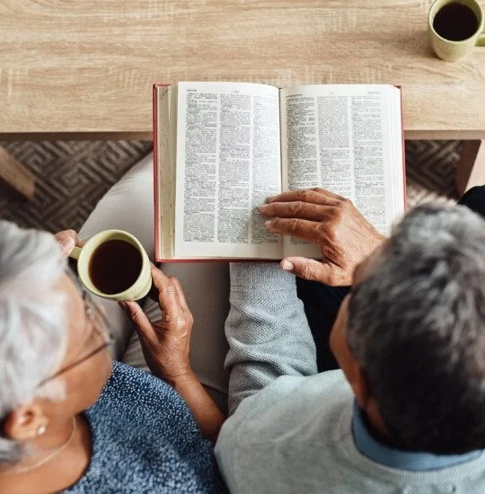 Two people reading a book together, both holding cups of coffee.