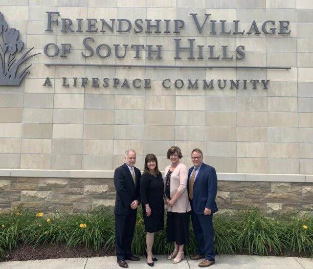People standing in front of Friendship Village of South Hills sign.