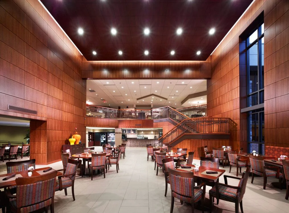 Spacious contemporary dining area with wooden panels and tables under bright ceiling lights.