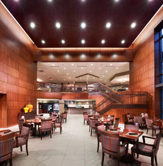 Spacious contemporary dining area with wooden panels and tables under bright ceiling lights.