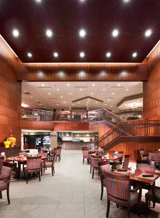 Spacious contemporary dining area with wooden panels and tables under bright ceiling lights.