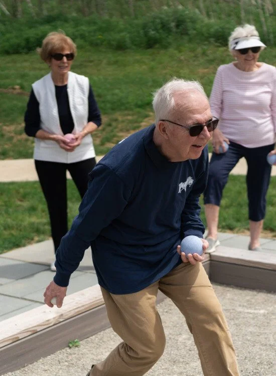 Elderly people playing bocce ball outdoors on a sunny day.