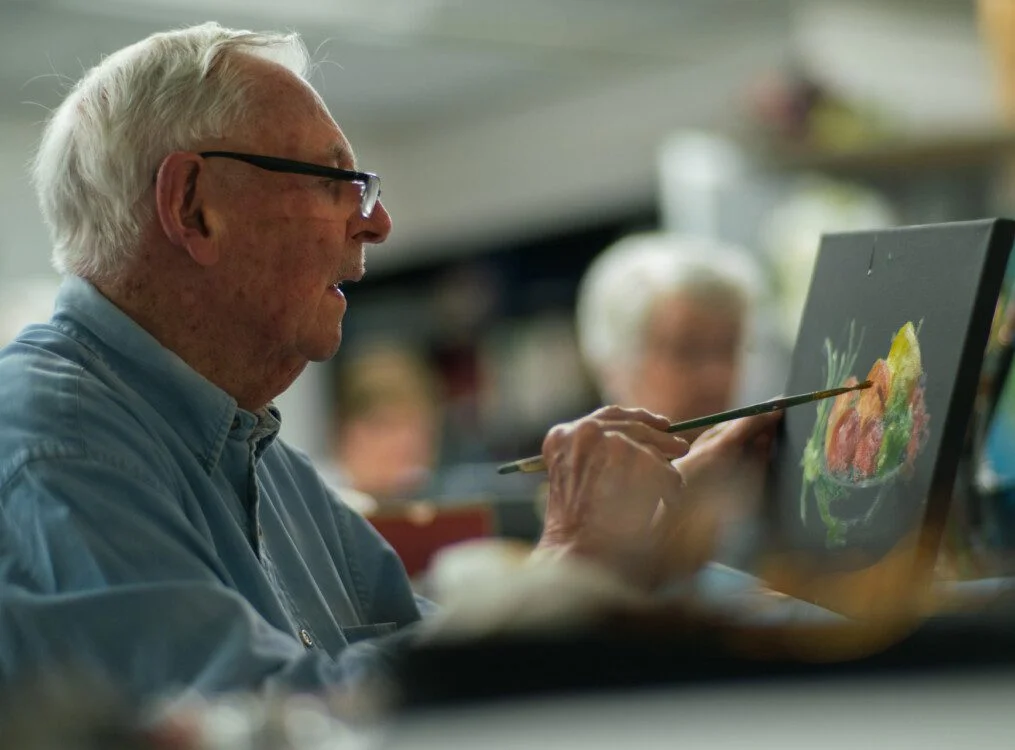 Elderly man painting colorful artwork on canvas indoors.