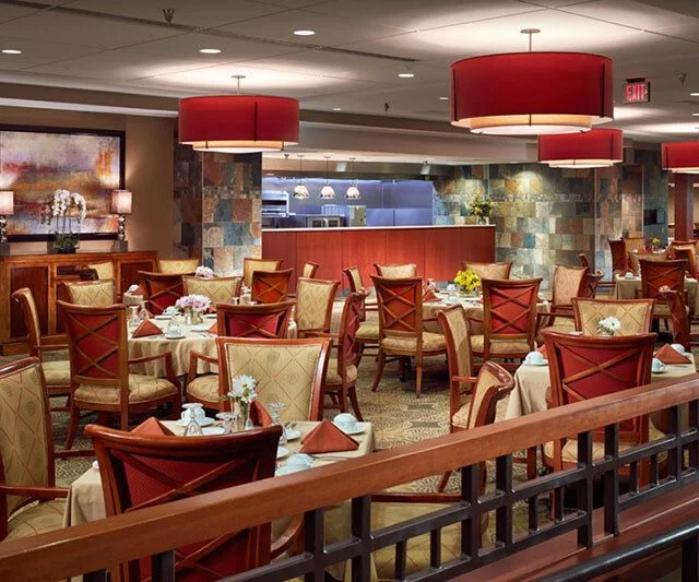 Elegant restaurant with red accents, set tables, and large overhead lights.