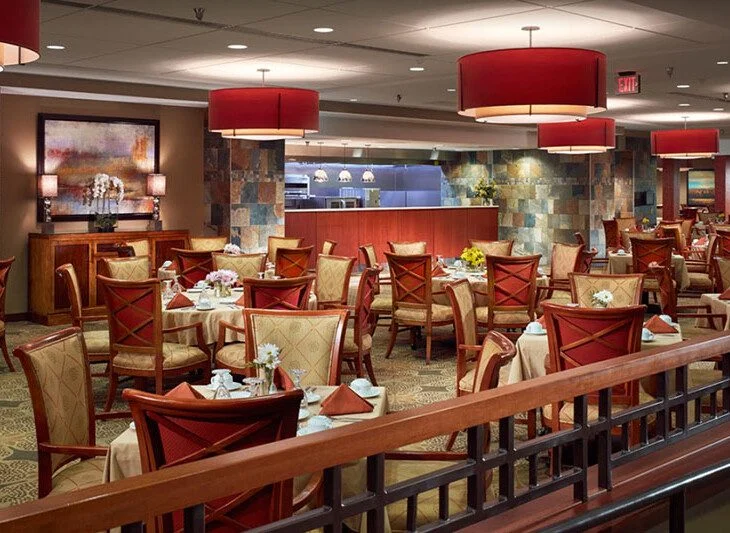 Elegant restaurant with red accents, set tables, and large overhead lights.