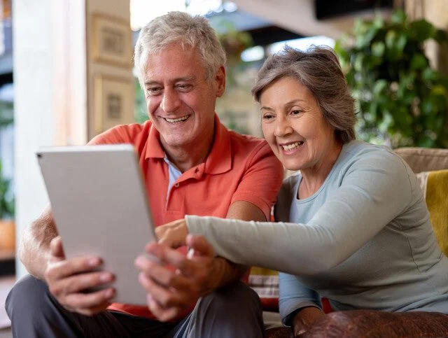 Senior couple smiling while looking at a tablet together at home.
