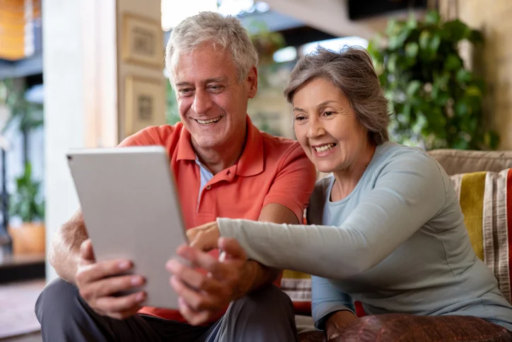 Senior couple smiling while looking at a tablet together at home.