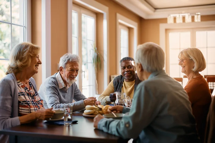 Five seniors happily chatting over breakfast at a sunlit table.