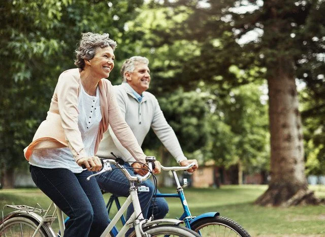 Elderly couple enjoying a leisurely bike ride in a lush park setting.