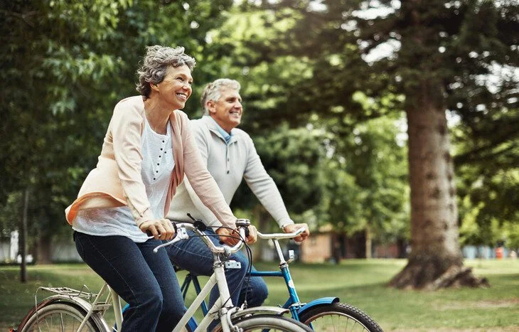 Elderly couple enjoying a leisurely bike ride in a lush park setting.