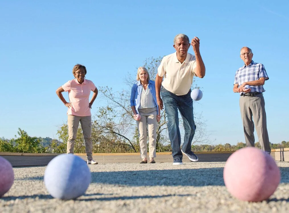 Four people playing bocce ball outdoors on a sunny day.
