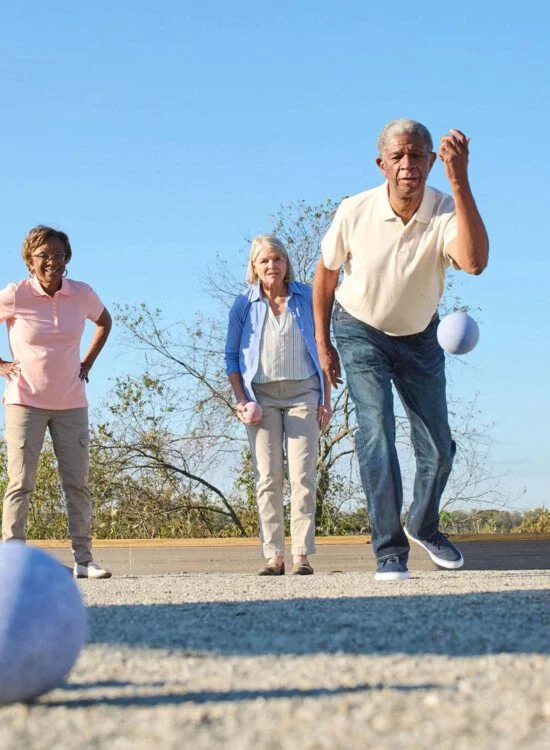 Four people playing bocce ball outdoors on a sunny day.