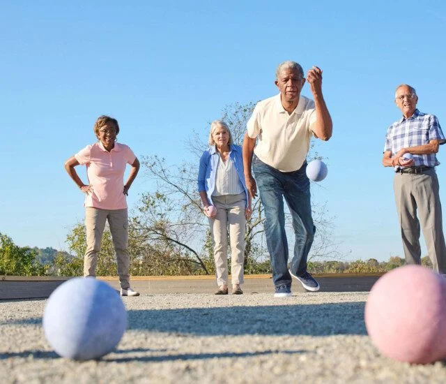Four people playing bocce ball outdoors on a sunny day.