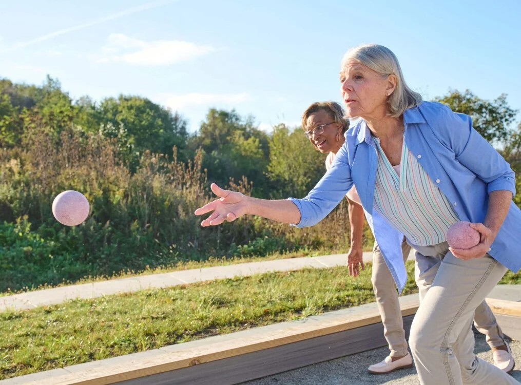 Two people play a ball game outdoors on a sunny day.