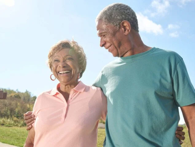 Older couple smiling and walking together outdoors on a sunny day.