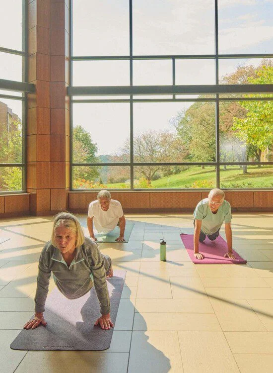 Older adults doing yoga indoors with large windows and garden view.