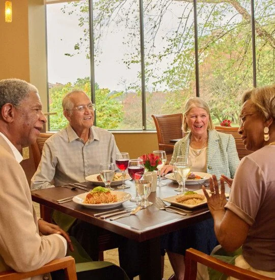 Four people dining together, smiling in a well-lit restaurant with large windows.