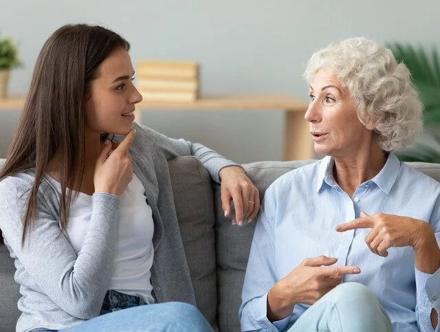 Two women sitting on a couch, engaged in lively conversation.