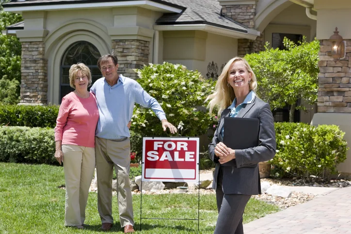 Realtor with clients in front of a house with a For Sale sign.