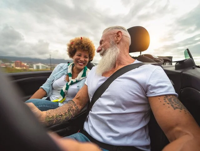 Couple smiling and driving in a convertible on a cloudy day.