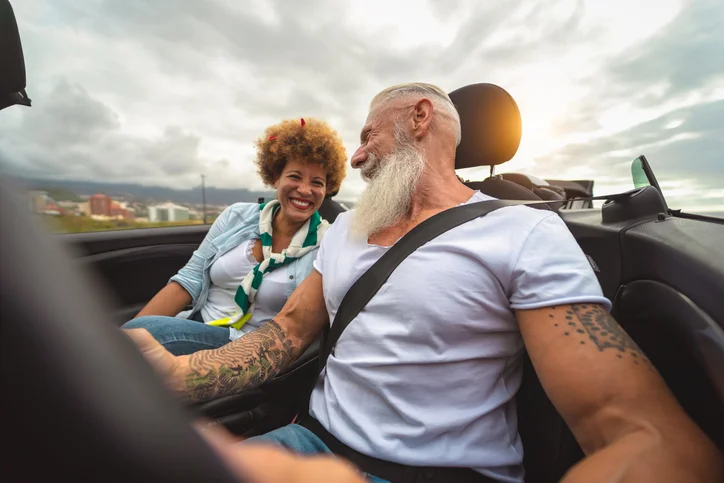 Couple smiling and driving in a convertible on a cloudy day.