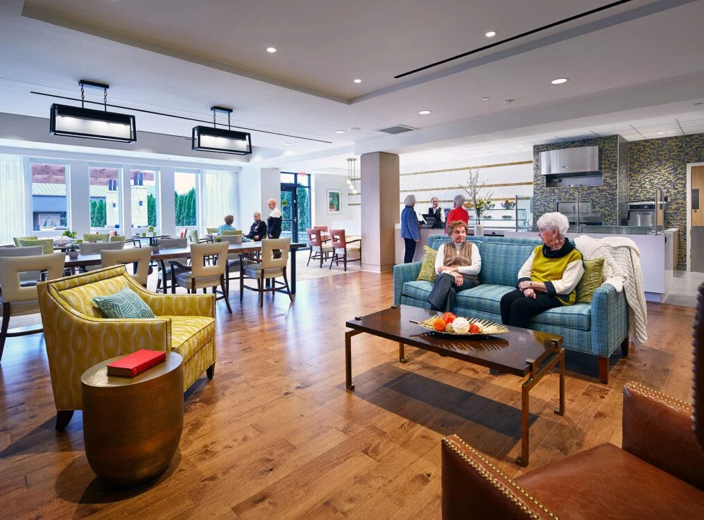 Modern lounge area with seniors chatting on sofas, tables, and chairs. Bright and airy atmosphere.