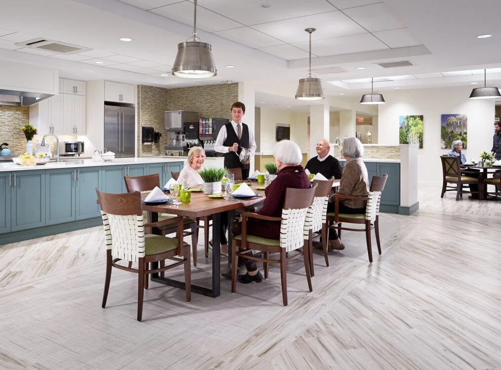 Dining area with seniors being served by a waiter in a modern kitchen setting.
