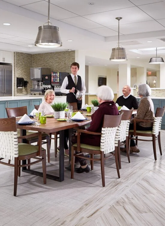Dining area with seniors being served by a waiter in a modern kitchen setting.
